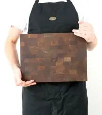 Ein Mann präsentiert ein exklusives Mooreiche-Schneidebrett (37x27 cm). Das Foto zeigt die dunkle Stirnholz-Oberfläche in der Ansicht von oben sowie die Seitenansicht zur Verdeutlichung der massiven Dicke von 4,3 cm.
